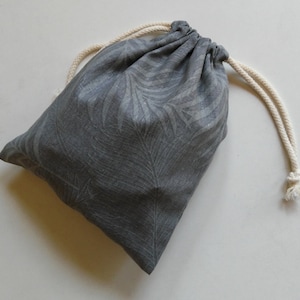 May include: A gray drawstring bag with a white leaf pattern. The bag is made of a soft, natural fabric and has a white drawstring.
