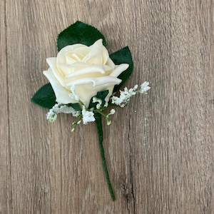 May include: A single white rose with green leaves and white baby's breath. The rose is a popular choice for wedding buttonholes.