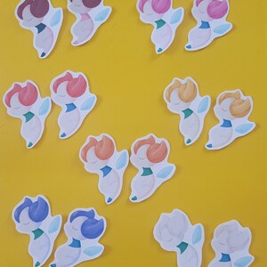 May include: A collection of colorful stickers featuring a stylized floral design. Each sticker has a white body, a colored head, and light blue accents. The heads are in various colors, including pink, orange, and blue, set against a yellow background.