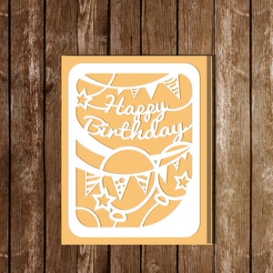 Pode incluir: Um cart&atilde;o branco com um design recortado que apresenta bal&otilde;es, estrelas e uma faixa que diz "Feliz anivers&aacute;rio".