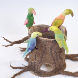 May include: Four felt birds perched on a brown felt tree stump. The birds are green, yellow, blue, and orange. The tree stump has a hole in the centre.