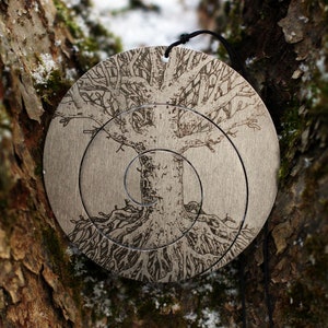 Puede incluir: Un colgante circular de plata con un diseño grabado detallado de un árbol con raíces y ramas. El colgante está colgado de un cordón negro.
