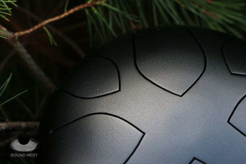 May include: A black steel tongue drum with a unique design featuring multiple indentations. The drum is made of steel and has a smooth, matte finish.