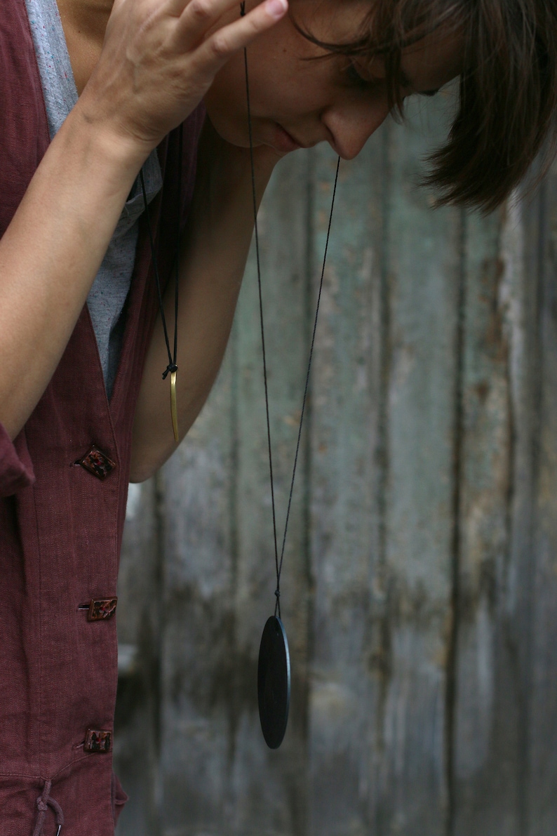 May include: A person wearing a maroon shirt with a black cord necklace and a black oval pendant.