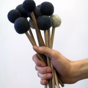 May include: A hand holds a bunch of wooden mallets with black and gray felt heads. The mallets are used for playing percussion instruments.