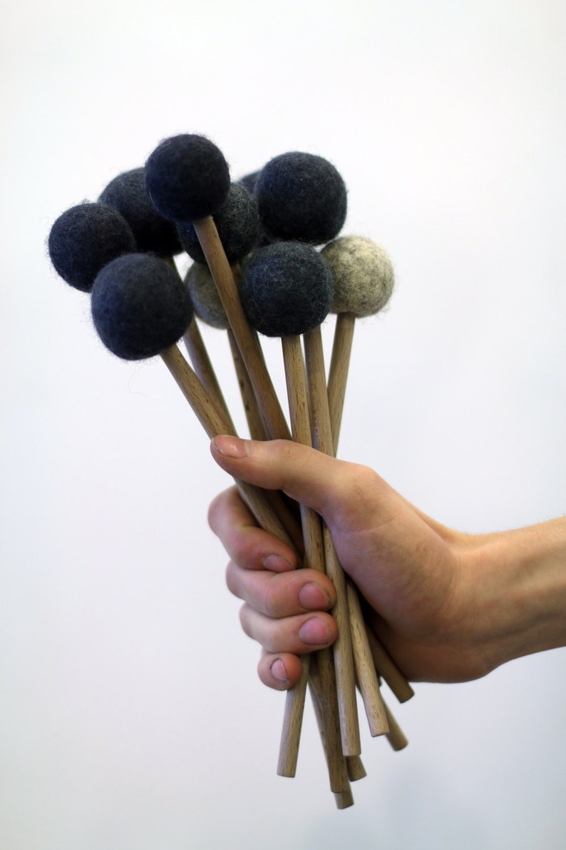May include: A hand holds a bunch of wooden mallets with black and gray felt heads. The mallets are used for playing percussion instruments.
