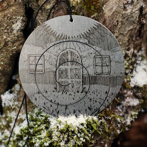 May include: A silver pendant with a detailed design of a house with a spiral staircase and windows. The pendant is hanging from a black cord and is surrounded by a natural background.