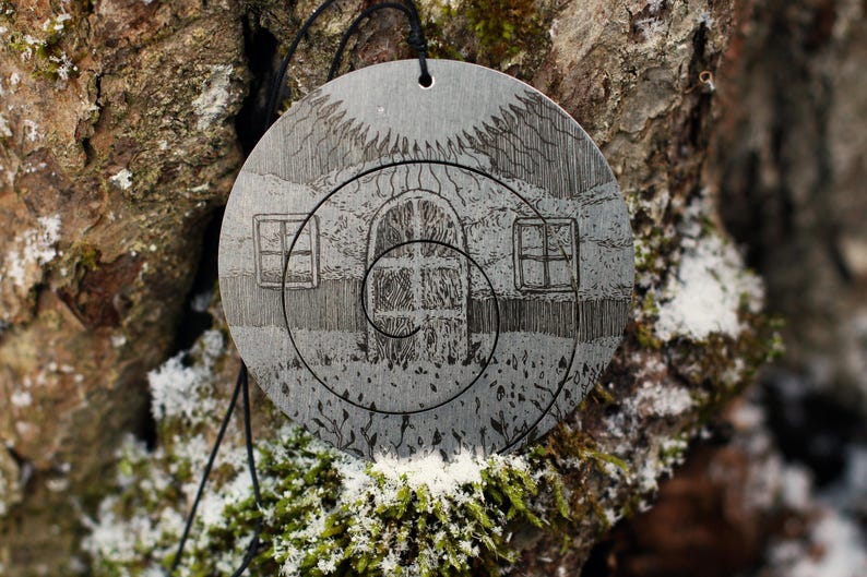 May include: A silver pendant with a detailed design of a house with a spiral staircase and windows. The pendant is hanging from a black cord and is surrounded by a natural background.