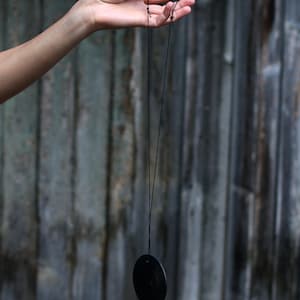 May include: A black disc pendant hanging from a black string held by a hand.