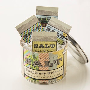 Könnte beinhalten: Eine Metalldose mit einem bunten Etikett, auf dem "Beautiful Briny Sea Salt Imaginary Friends Sample Pack" steht, und sechs kleine Päckchen Salz enthält. Die Dose hat einen Deckel, der offen ist, und die Salzpäckchen sind im Inneren sichtbar.
