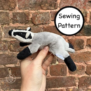 May include: A plush badger toy with gray fur, black legs and a white and black striped head. The toy is held in a hand. A white circle with the words "Sewing Pattern" is in the background.