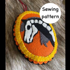 May include: A felt sewing pattern featuring a horse skeleton design. The horse head is black and white, set against an orange background, and framed with yellow and black scalloped edges. The text "Sewing pattern" is in a white circle.
