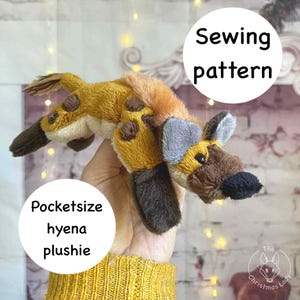 Puede incluir: Un peluche de hiena de bolsillo hecho a mano con un patrón de costura. El peluche presenta un cuerpo marrón con manchas marrones, una cara marrón y negra y orejas grises. El texto "Sewing pattern" y "Pocketsize hyena plushie" está en círculos blancos.
