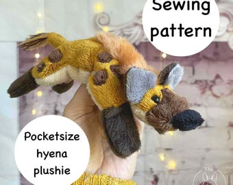 May include: A handmade, pocket-sized hyena plushie with a sewing pattern. The plushie features a tan body with brown spots, a brown and black face, and gray ears. The text "Sewing pattern" and "Pocketsize hyena plushie" are in white circles.