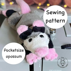 May include: A small, plush opossum toy with grey fur, pink paws, and black details. The image includes the text "Pocketsize opossum" and "Sewing pattern". The Christmas Lady logo is also visible.
