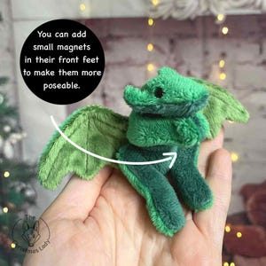 Puede incluir: Un drag&oacute;n de peluche verde con grandes alas y peque&ntilde;os ojos negros. El texto de la imagen dice: "Puedes a&ntilde;adir peque&ntilde;os imanes en sus patas delanteras para que sean m&aacute;s manejables." El drag&oacute;n es un art&iacute;culo hecho a mano.