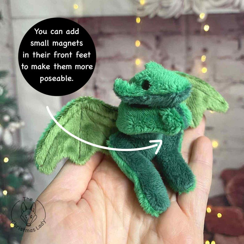 Puede incluir: Un drag&oacute;n de peluche verde con grandes alas y peque&ntilde;os ojos negros. El texto de la imagen dice: "Puedes a&ntilde;adir peque&ntilde;os imanes en sus patas delanteras para que sean m&aacute;s manejables." El drag&oacute;n es un art&iacute;culo hecho a mano.