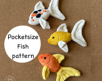 May include: Three plush fish toys in white, yellow, and orange with white accents. One fish has black and orange spots. The text "Pocketsize Fish pattern" is in a white circle. The fish are on a brown surface.