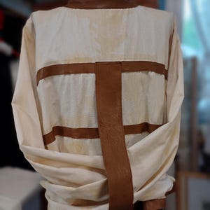 May include: Cream-colored jacket with brown leather accents. The jacket features a brown leather collar and horizontal and vertical straps across the back. The jacket is displayed on a mannequin.