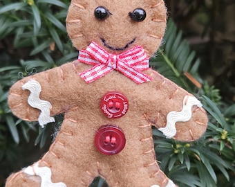 May include: A felt gingerbread man Christmas ornament with black bead eyes, a red and white striped bow tie, and red buttons. The gingerbread man has white trim on the arms and legs and is hanging from a red ribbon.