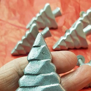 May include: Silver metal Christmas tree shaped drawer pull. The tree has a textured surface and is a 3D design.