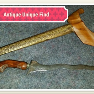 May include: Two antique daggers with ornate gold and silver detailing. The larger dagger has a wooden scabbard with intricate carvings. The smaller dagger has a wooden handle and a curved blade.