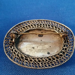 May include: An antique oval brooch with a filigree border. The brooch has a pin on the back for attachment. The center of the brooch has a faded image. The metal has a tarnished appearance.