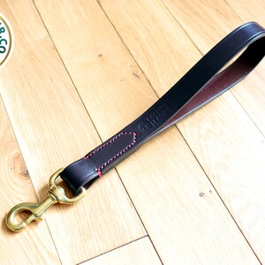 May include: A black leather dog leash with red stitching and a brass hook. The leash is embossed with the text "Ross Leather Co. UK".