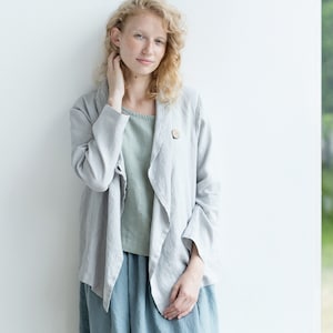 May include: A woman wearing a light gray linen jacket with a wooden button. She is wearing a light green top and a light blue skirt.