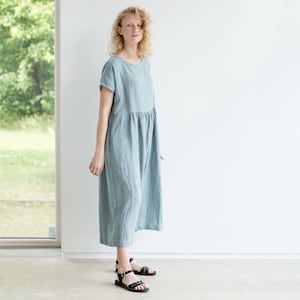 May include: A light blue linen dress with a loose fit and short sleeves. The dress has a gathered waist and falls to the mid-calf.