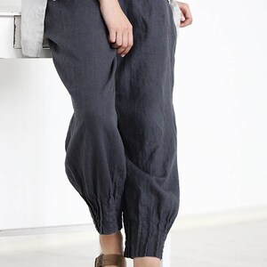 Puede incluir: Pantal&oacute;n de lino gris con un pu&ntilde;o el&aacute;stico fruncido en el tobillo. El pantal&oacute;n se lleva con sandalias de cuero marr&oacute;n.