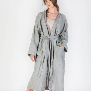 May include: A long, striped, gray linen robe with a sash tie and pockets. The robe is worn by a person with long brown hair. The person is wearing sandals.
