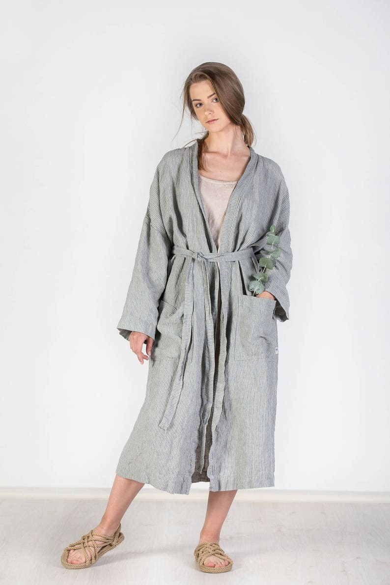 May include: A long, striped, gray linen robe with a sash tie and pockets. The robe is worn by a person with long brown hair. The person is wearing sandals.