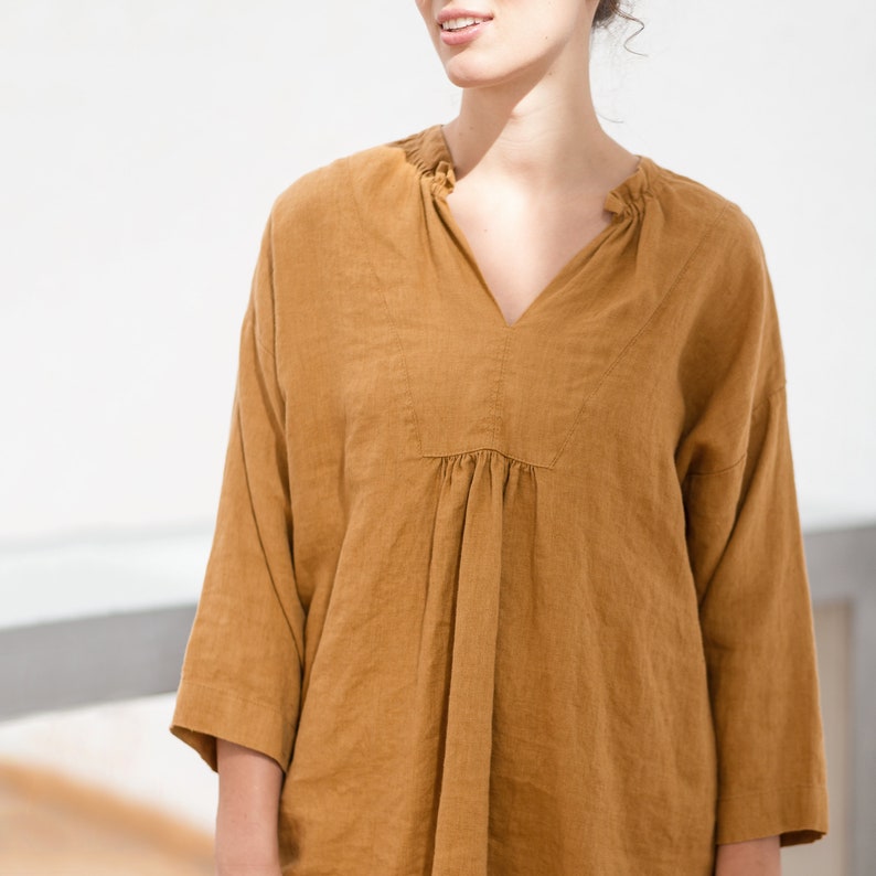 May include: A loose-fitting, brown linen tunic with a V-neck and a gathered waist.