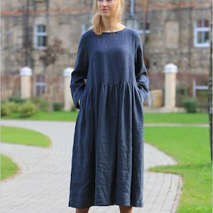 May include: A long-sleeved, navy blue linen dress with a gathered waist and pockets. The dress is worn by a person with brown boots.
