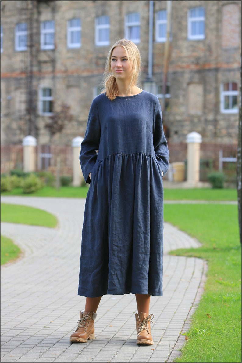 May include: A long-sleeved, navy blue linen dress with a gathered waist and pockets. The dress is worn by a person with brown boots.