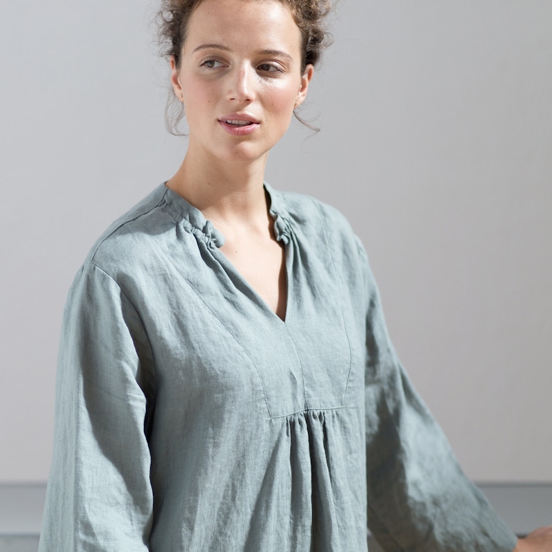 May include: A light blue linen shirt with a V-neck and a gathered waist.
