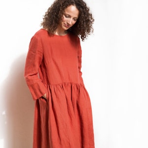 May include: A long-sleeved, rust-colored linen dress with a gathered skirt and pockets.