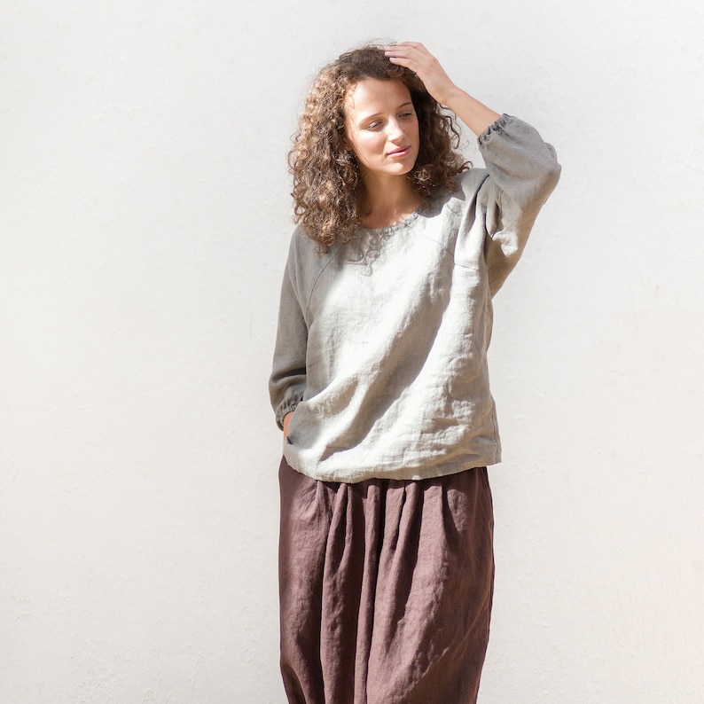 May include: A woman wearing a light gray linen top with a brown linen skirt. The top has a relaxed fit and a slightly gathered neckline. The skirt is a wide-leg style with a high waist.