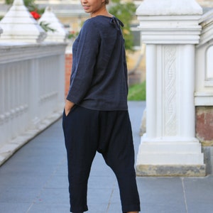 May include: A woman wearing a dark blue long-sleeved shirt and dark blue pants with a loose, baggy fit. She is standing on a paved surface in front of a white stone structure.