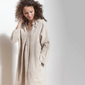 May include: A woman wearing a beige linen dress with a V-neck and a gathered waist.