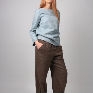 May include: A woman wearing a light blue linen top and brown linen pants with cuffed hems. She is wearing beige lace-up shoes.