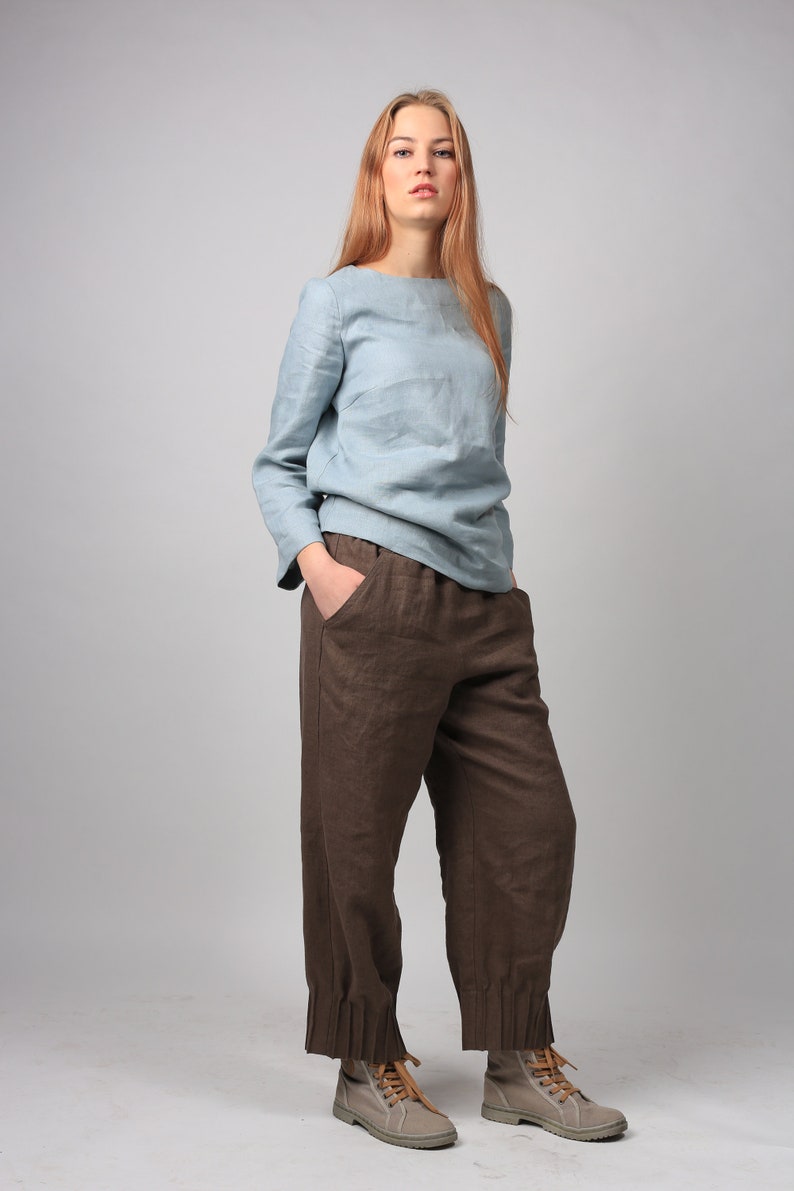 May include: A woman wearing a light blue linen top and brown linen pants with cuffed hems. She is wearing beige lace-up shoes.