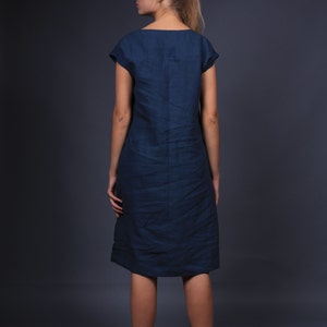 May include: A woman wearing a dark blue linen dress with short sleeves. The dress is knee-length and has a simple, straight silhouette.