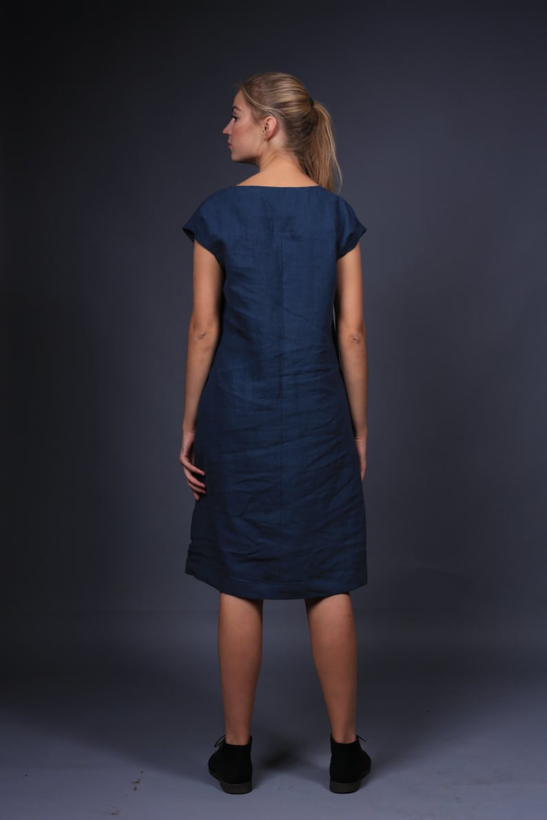 May include: A woman wearing a dark blue linen dress with short sleeves. The dress is knee-length and has a simple, straight silhouette.