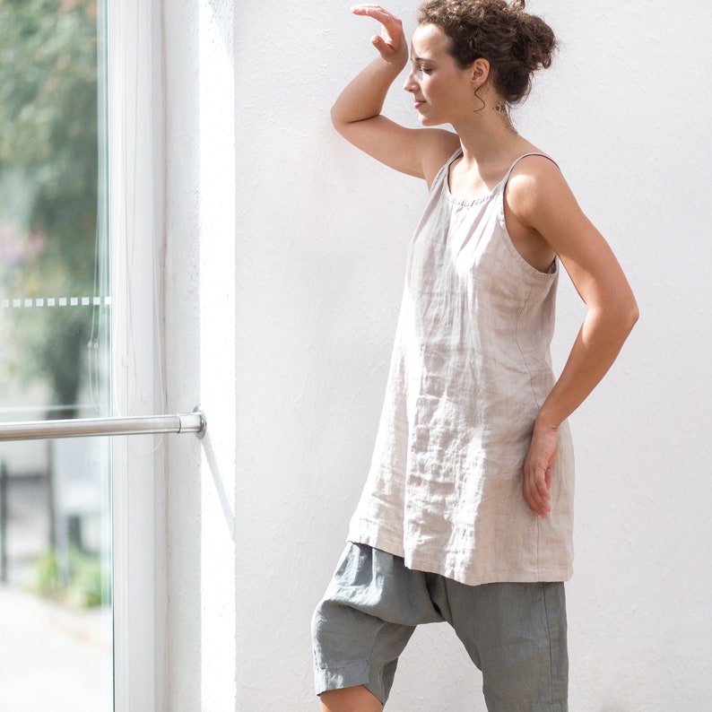 May include: A woman wearing a light beige linen sleeveless top with a loose fit and a pair of gray linen pants.