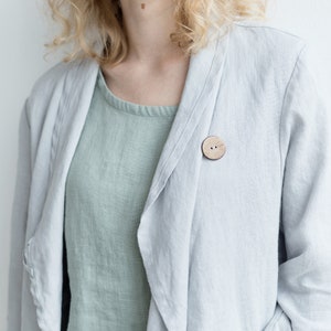May include: A light gray linen jacket with a wooden button closure. The jacket is open and the collar is folded down.