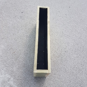 May include: A long, rectangular wooden planter with a natural wood finish. The interior is lined with black fabric. The planter is designed to be long and narrow, suitable for plants. The box is empty and ready for planting.
