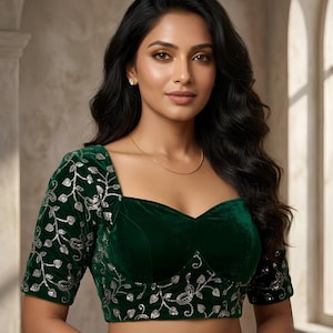 May include: A dark green velvet blouse featuring a sweetheart neckline and short sleeves. The garment is adorned with intricate silver sequin embroidery in a vine and leaf pattern across the sleeves and the lower front hemline.