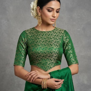 May include: A vibrant green blouse featuring a gold floral brocade pattern, elbow-length sleeves, and a pointed hemline. The garment has a round neckline and gold piping along the edges, paired with a matching solid green fabric draped below.